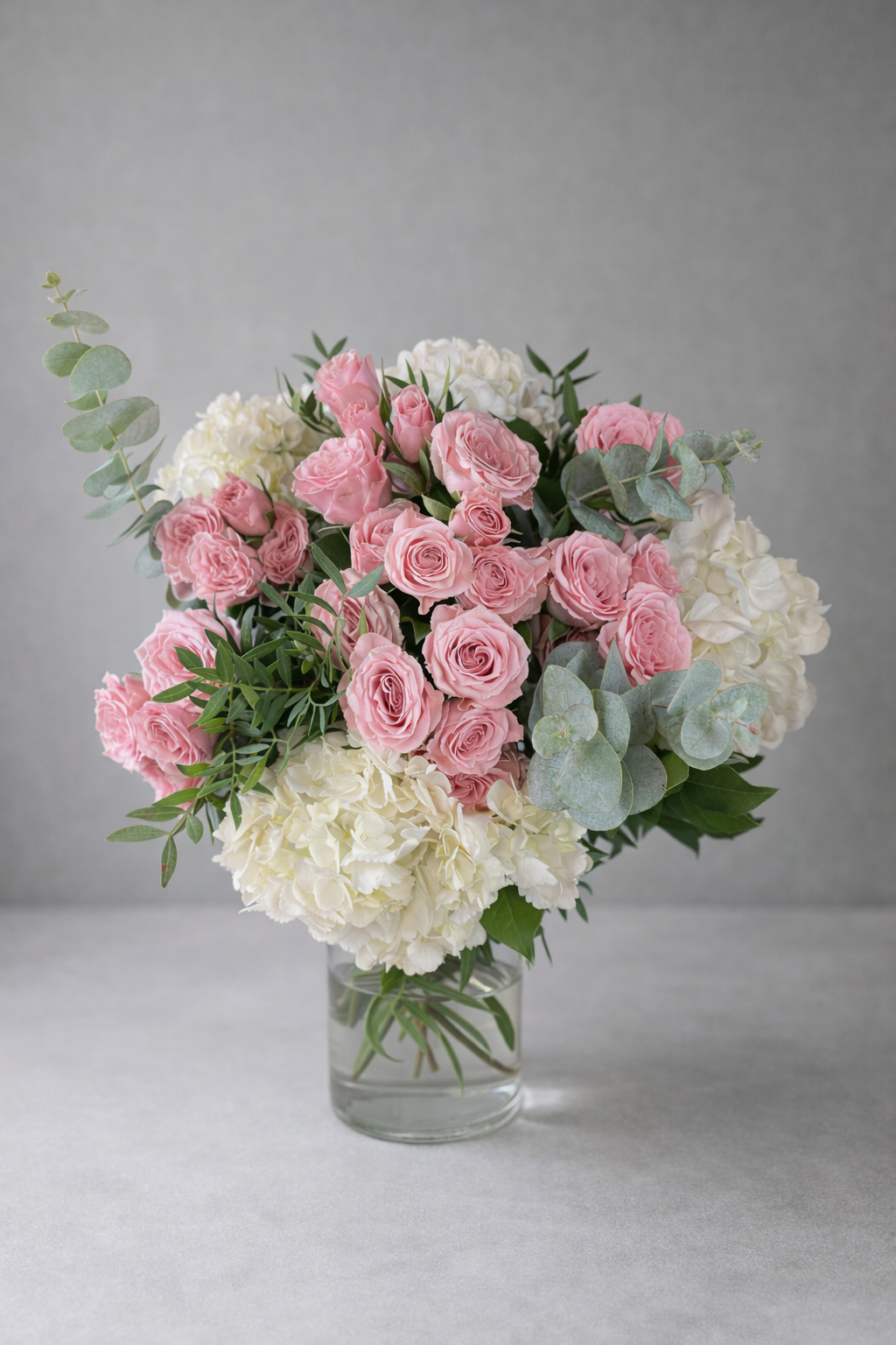 Pink roses and white hydrangea arrangement in a vase, the compact scale suited to a hospital bedside table