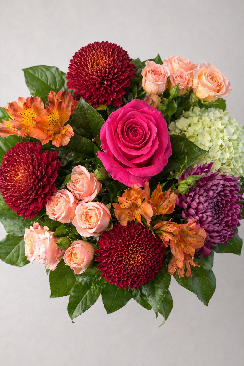 Top view of a luxury autumn bouquet with layered blooms and foliage, featuring a hot pink rose, peach spray roses, burgundy pompon chrysanthemums, mauve chrysanthemum, orange alstroemeria and soft green hydrangea, styled as elegant luxury flowers Montreal.