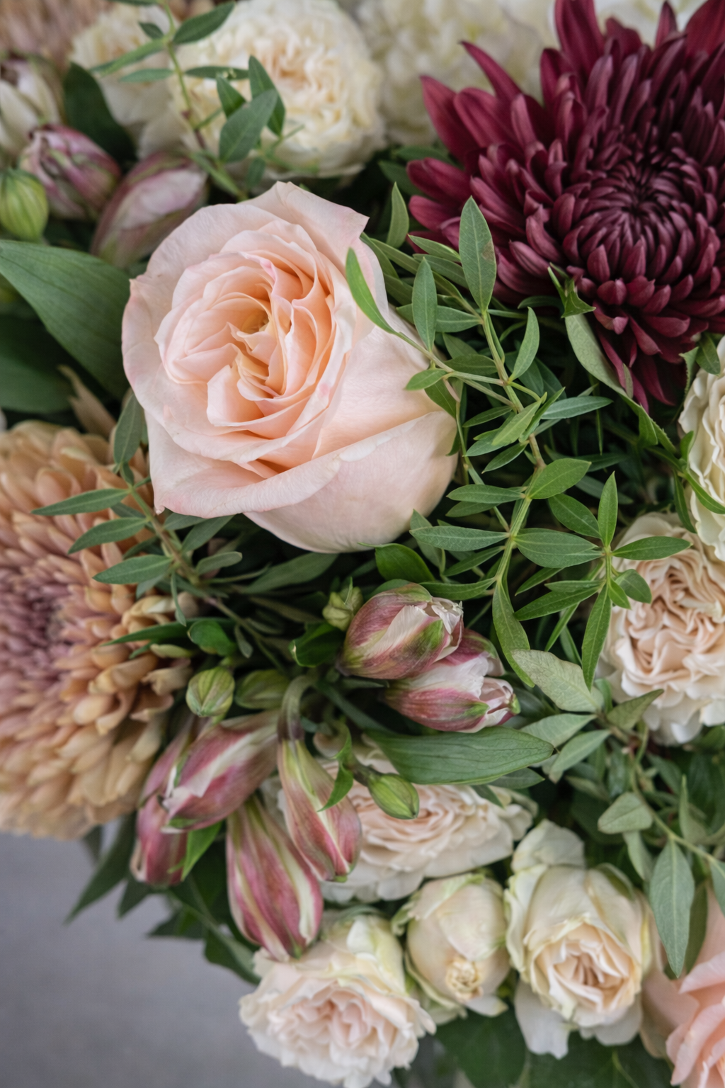 Botanical close-up of blush rose, burgundy chrysanthemum, cream spray roses and foliage with soft natural texture and elegant detail