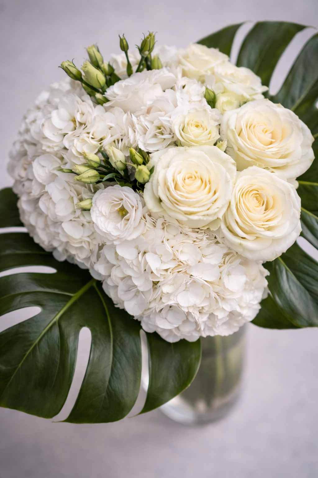 Top view of a white bouquet with hydrangeas, ivory roses, lisianthus buds and glossy monstera foliage, styled with soft depth of field for luxury flowers Montreal product photography.