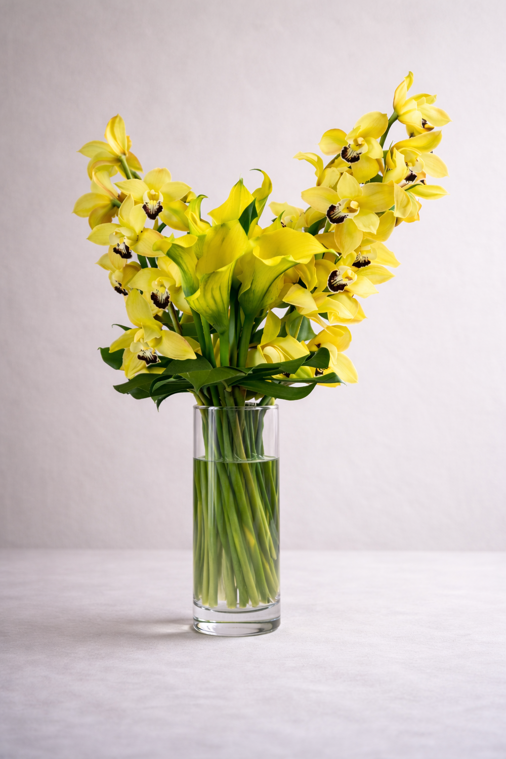 Luxury yellow cymbidium orchid and calla lily arrangement in clear glass vase, front studio view, Montreal florist contemporary design