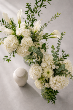 Top view of luxury flowers Montreal for an urn tribute, with white calla lilies, hydrangeas, a single chrysanthemum, eucalyptus and Italian ruscus arranged in clear vases around a contemporary urn.
