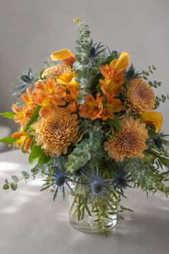 Close-up of orange alstroemeria, peach chrysanthemums, yellow calla lilies, eucalyptus and blue thistle in a luxury Montreal bouquet.
