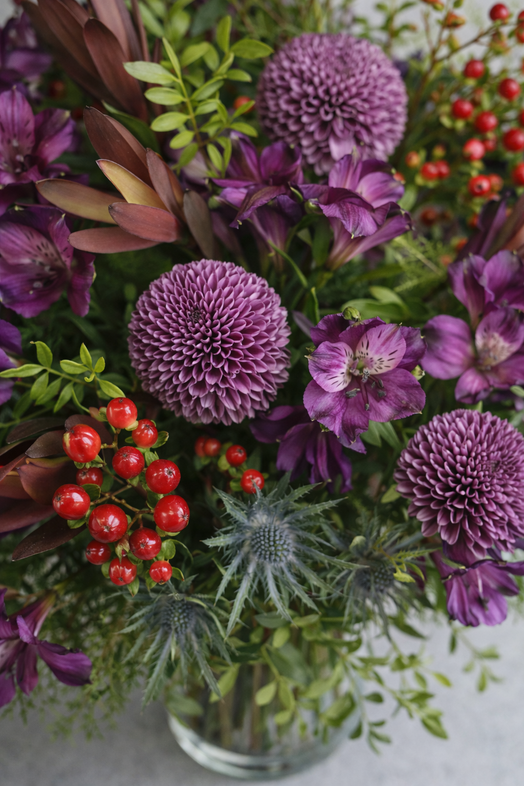 Top view of a purple flower bouquet with textured blooms, foliage, berries, and thistle in a refined Montreal florist style