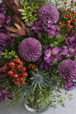 Top view of a purple flower bouquet with textured blooms, foliage, berries, and thistle in a refined Montreal florist style