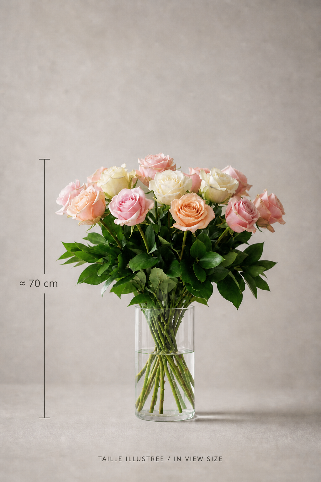 Pastel rose floral arrangement in a clear glass vase with lush green foliage, shown with an approximate 70 cm size reference for scale in an elegant studio composition by a luxury florist Montreal.