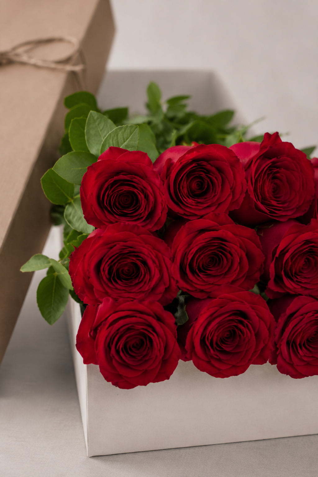Close-up of velvety red rose blooms and fresh green foliage inside a white floral box, capturing petal texture and botanical detail in a luxury flowers Montreal style.