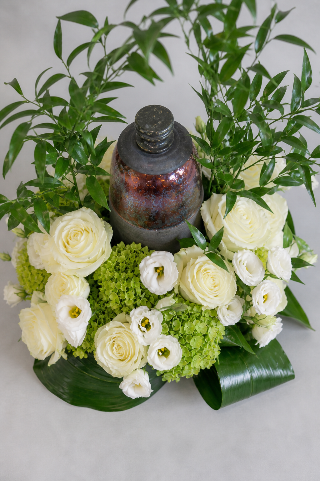 Top view of a premium urn tribute featuring ivory roses, white lisianthus, fresh green hydrangea and airy foliage, styled as an elegant floral arrangement Montreal.