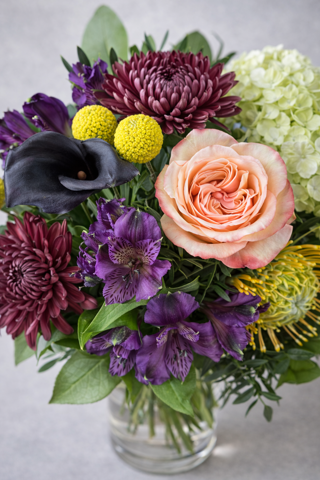 Top view floral detail of a luxury bouquet with peach rose, dark calla lily, purple alstroemeria, burgundy chrysanthemums and green hydrangea.
