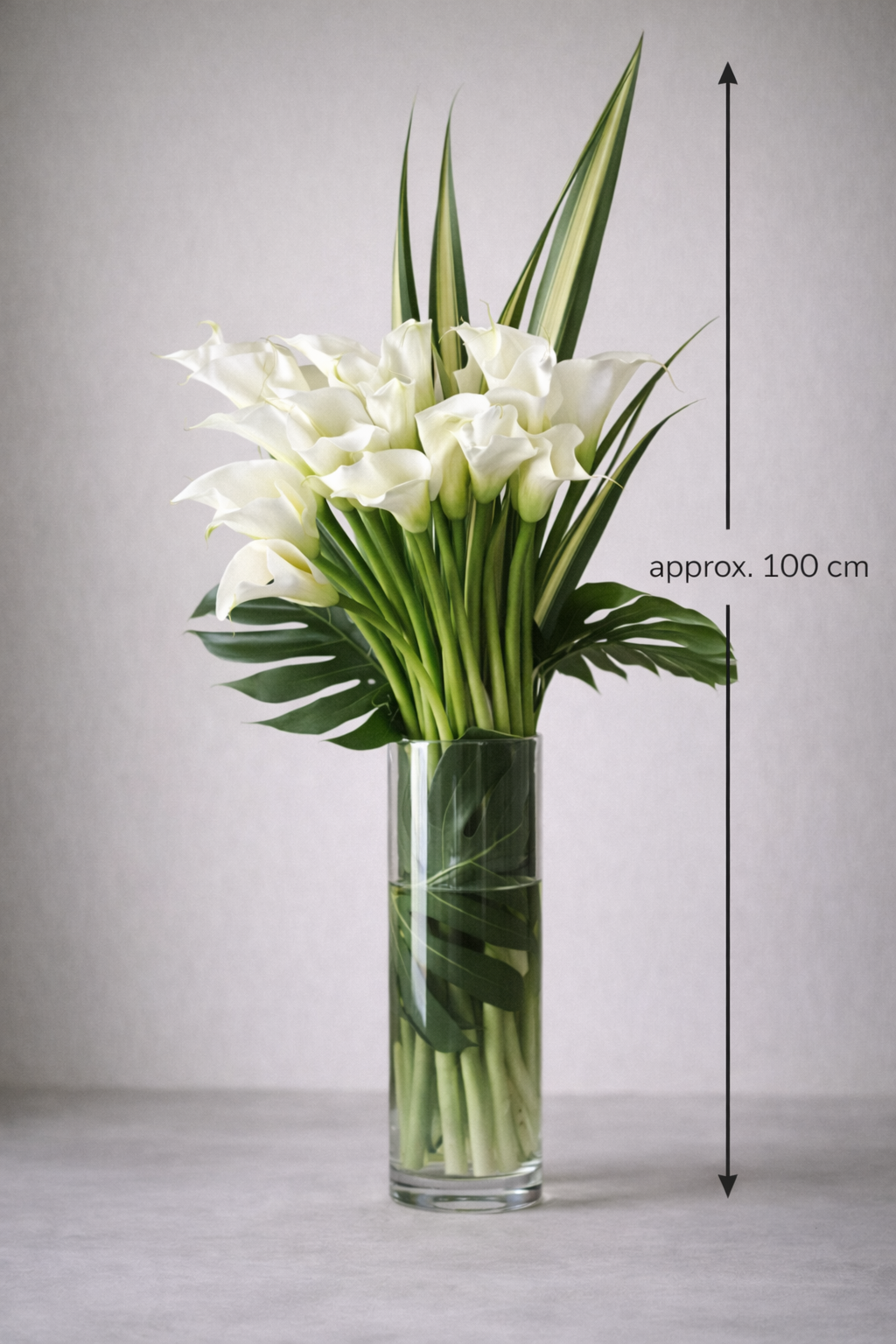 Luxury white calla lily bouquet approximately 100 cm tall in clear glass vase, contemporary high-end floral arrangement by Montreal florist.