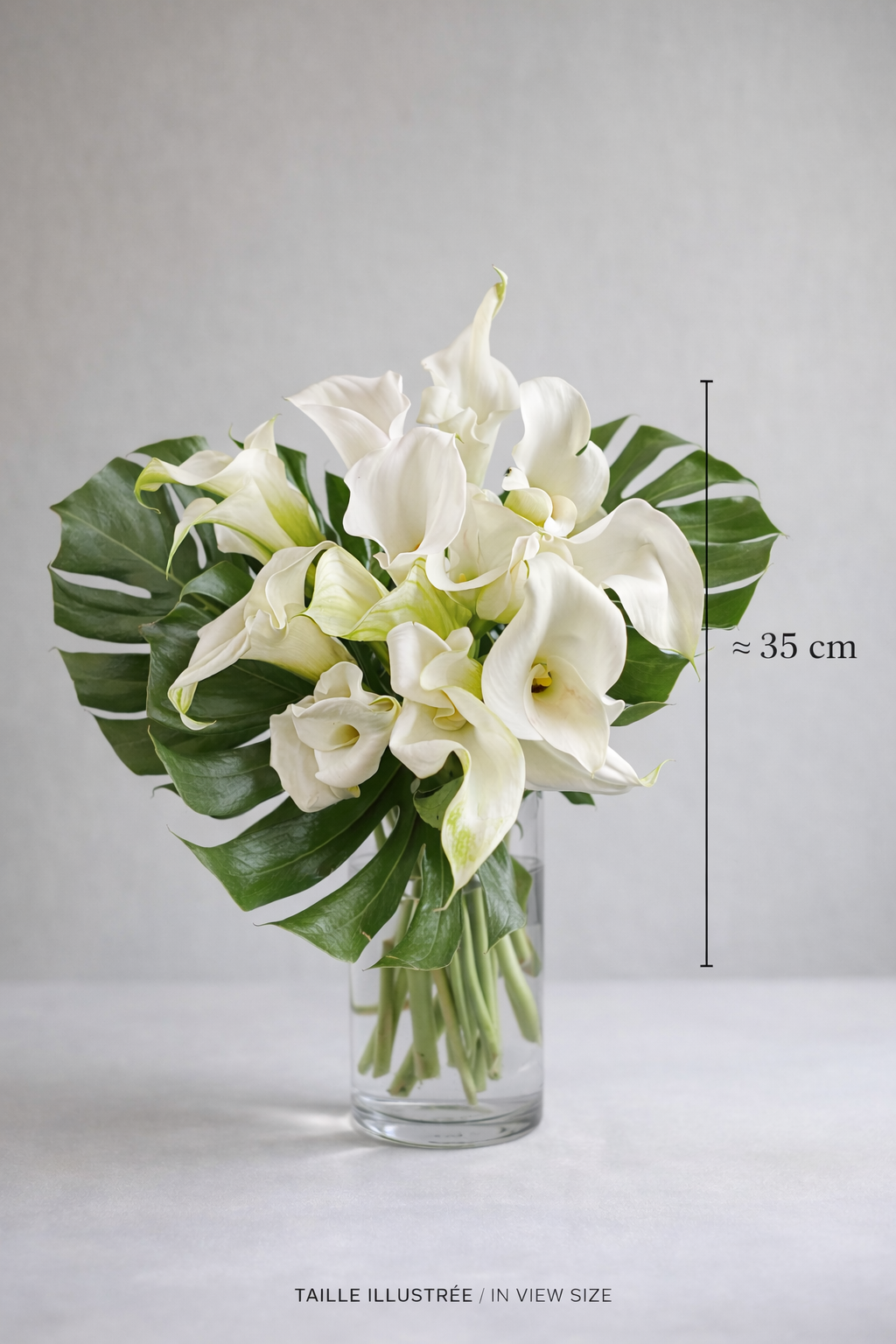 White calla lily bouquet with monstera leaves, approximately 35 cm tall, shown in a clear vase for size reference, Montreal florist