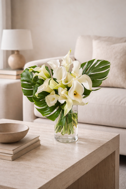 White calla lily bouquet styled in a contemporary neutral interior, arranged in a clear glass vase with monstera leaves, Montreal florist