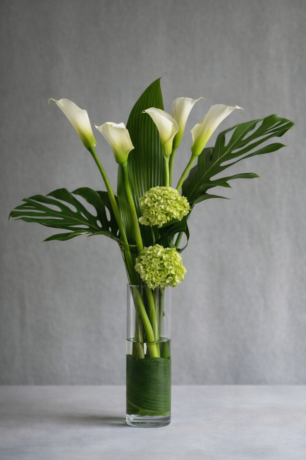White calla lily and green hydrangea floral arrangement in a narrow clear glass vase, photographed front-facing in an elegant editorial style by a luxury florist in Montreal.