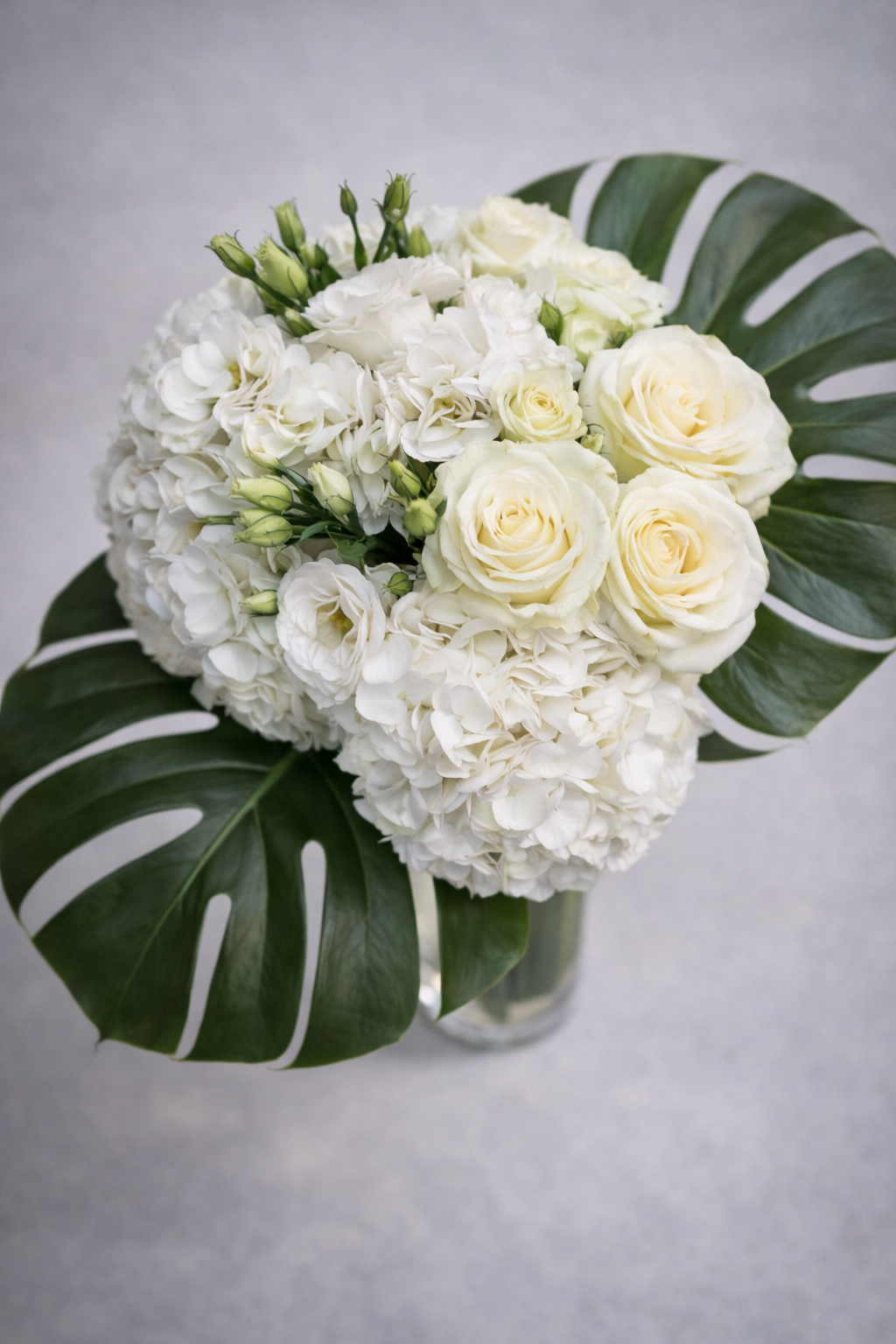 Botanical close-up of white roses, hydrangea petals and lisianthus buds with visible monstera leaf texture, captured as a refined floral arrangement Montreal detail shot.
